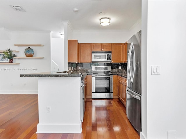 kitchen featuring dark wood-type flooring, dark stone countertops, ornamental molding, appliances with stainless steel finishes, and backsplash