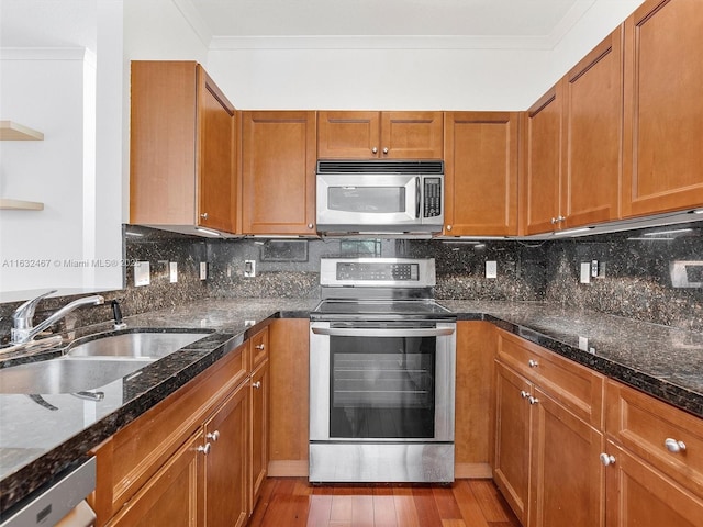 kitchen with appliances with stainless steel finishes, sink, decorative backsplash, ornamental molding, and light hardwood / wood-style floors