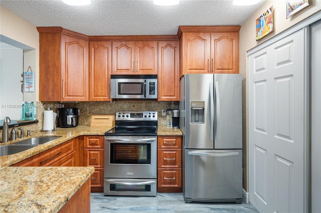 kitchen featuring light stone countertops, appliances with stainless steel finishes, a textured ceiling, and sink