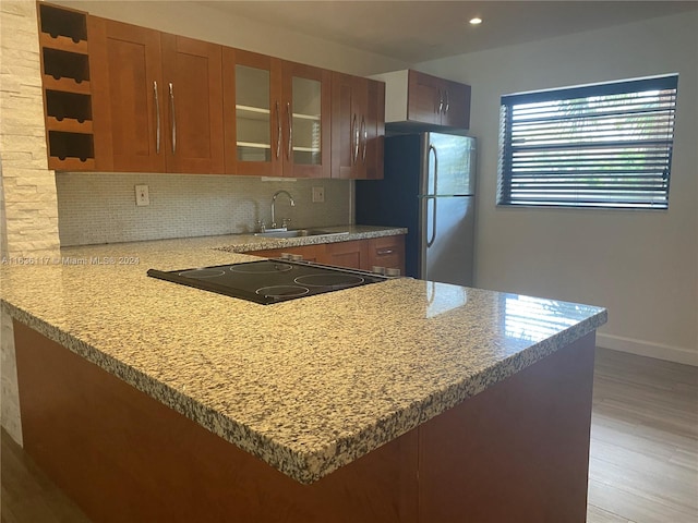 kitchen featuring sink, light hardwood / wood-style floors, stainless steel refrigerator, kitchen peninsula, and backsplash