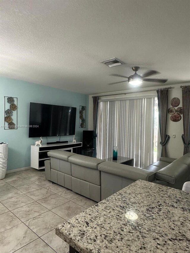 living room with ceiling fan, light tile patterned flooring, and a textured ceiling