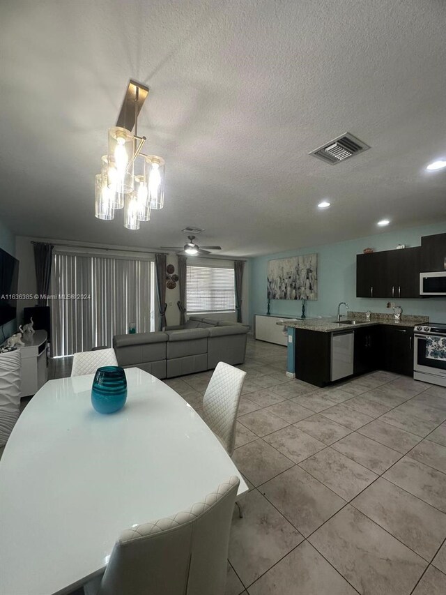 tiled dining space with ceiling fan with notable chandelier, a textured ceiling, and sink