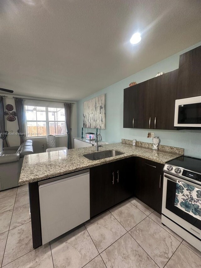 kitchen with light stone counters, kitchen peninsula, light tile patterned floors, electric range, and sink