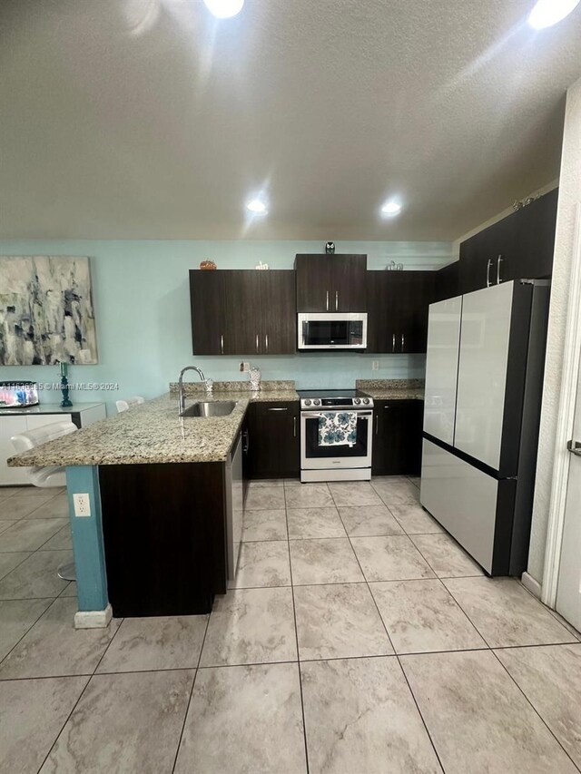 kitchen with light tile patterned floors, appliances with stainless steel finishes, sink, and light stone countertops