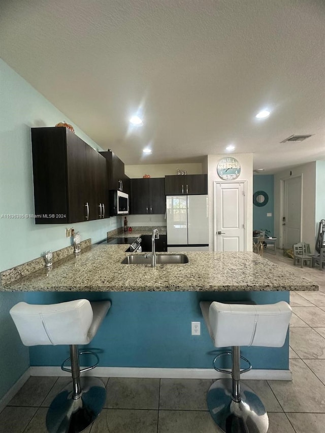 kitchen featuring a textured ceiling, light stone countertops, sink, white fridge, and light tile patterned flooring