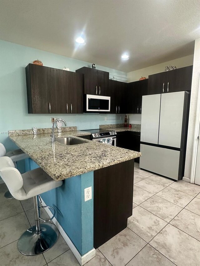 kitchen with white appliances, a kitchen bar, sink, light stone counters, and kitchen peninsula