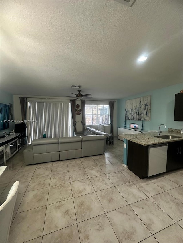 kitchen featuring a textured ceiling, light tile patterned flooring, stainless steel dishwasher, ceiling fan, and sink