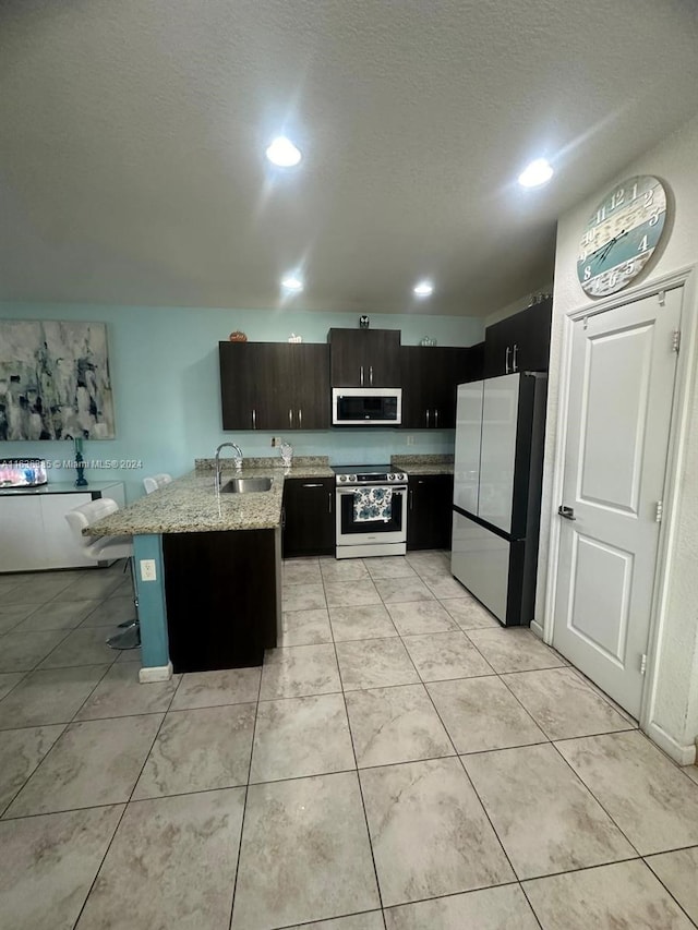 kitchen featuring light stone countertops, light tile patterned flooring, a kitchen breakfast bar, stainless steel appliances, and sink