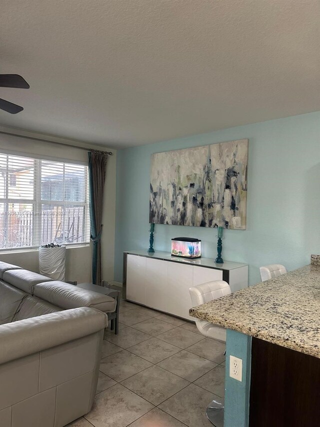 living room with ceiling fan, light tile patterned flooring, and a textured ceiling