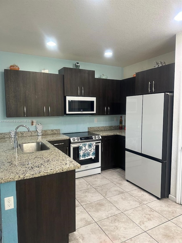 kitchen with sink, stainless steel range with electric cooktop, fridge, light stone counters, and dark brown cabinetry