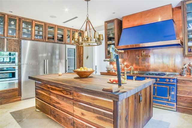 kitchen with butcher block countertops, appliances with stainless steel finishes, range hood, a warming drawer, and glass insert cabinets