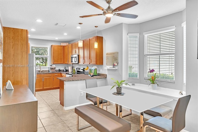 kitchen with hanging light fixtures, kitchen peninsula, dark stone counters, light tile patterned floors, and appliances with stainless steel finishes