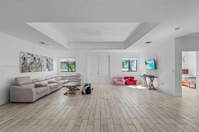 living room featuring light wood-type flooring, a raised ceiling, and plenty of natural light