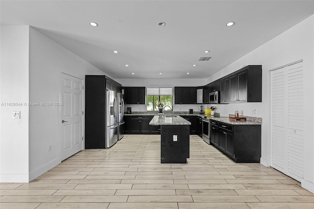 kitchen featuring appliances with stainless steel finishes, sink, light stone counters, light hardwood / wood-style floors, and a kitchen island