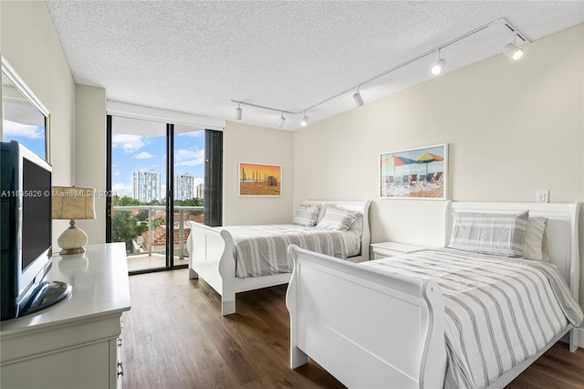 bedroom featuring access to exterior, a textured ceiling, rail lighting, and dark wood-type flooring