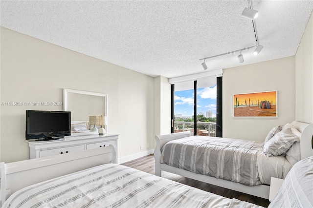 bedroom featuring hardwood / wood-style floors, rail lighting, a textured ceiling, and a wall of windows