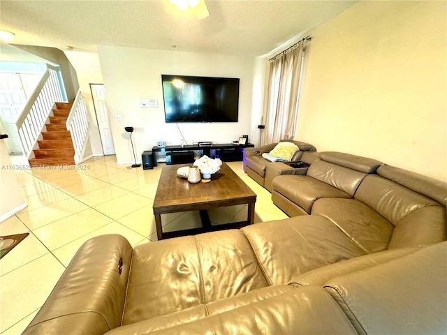 living room featuring a ceiling fan, a textured ceiling, tile patterned flooring, baseboards, and stairs