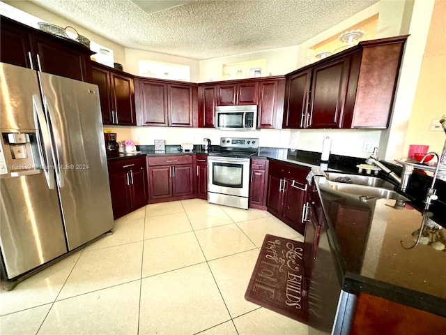 kitchen featuring a textured ceiling, light tile patterned floors, a sink, appliances with stainless steel finishes, and reddish brown cabinets