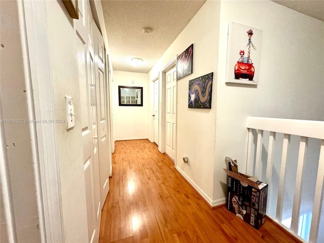 corridor with a textured ceiling, light wood finished floors, and baseboards