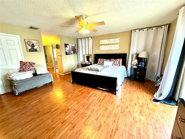 bedroom with light wood finished floors, ceiling fan, visible vents, and a textured ceiling