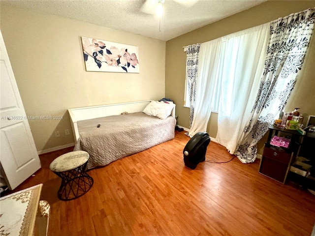 bedroom featuring baseboards, a textured ceiling, a ceiling fan, and wood finished floors