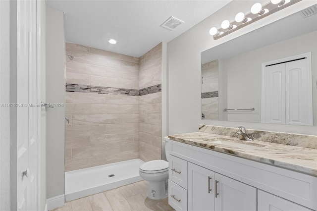 bathroom with hardwood / wood-style floors, vanity, toilet, and tiled shower