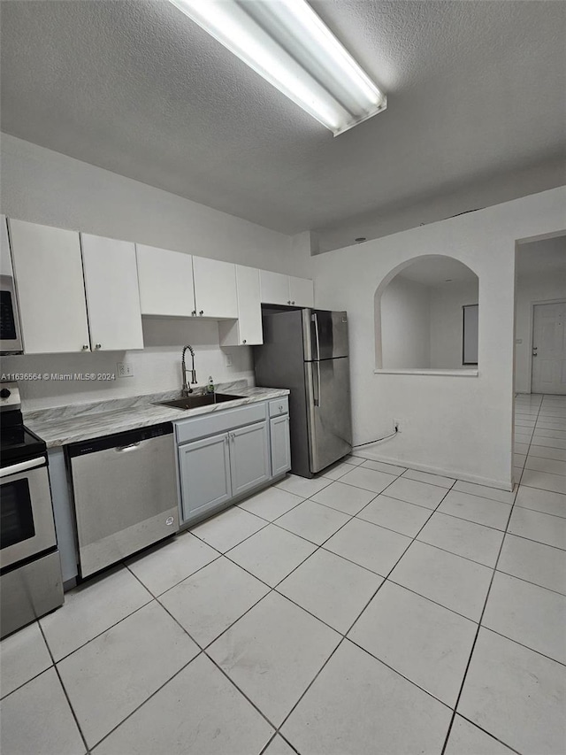 kitchen featuring light tile patterned floors, appliances with stainless steel finishes, sink, and white cabinetry