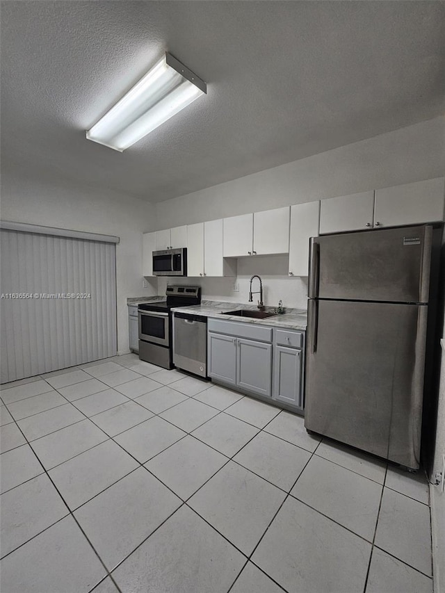 kitchen with gray cabinets, stainless steel appliances, white cabinetry, light tile patterned floors, and sink