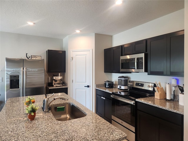 kitchen with light stone countertops, appliances with stainless steel finishes, sink, and a textured ceiling