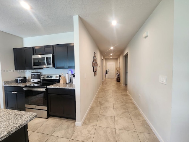 kitchen with a textured ceiling, light tile patterned floors, light stone counters, and stainless steel appliances