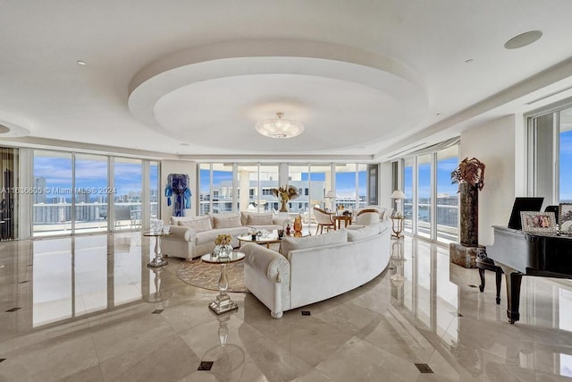 living room with expansive windows, a water view, light tile patterned floors, and a tray ceiling