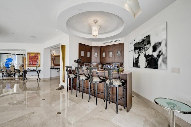 bar featuring decorative backsplash, dark brown cabinets, and a raised ceiling