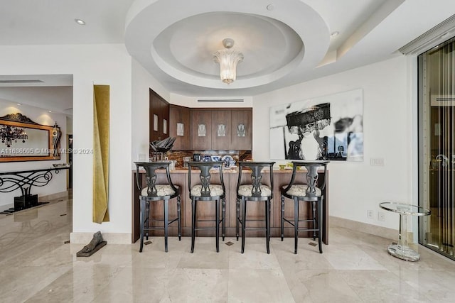 bar with light tile patterned flooring, dark brown cabinets, and a tray ceiling