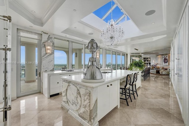 kitchen featuring white cabinetry, a chandelier, an island with sink, a raised ceiling, and light tile patterned floors