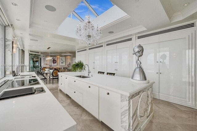 kitchen featuring light tile patterned flooring, a notable chandelier, white cabinets, a kitchen island with sink, and sink