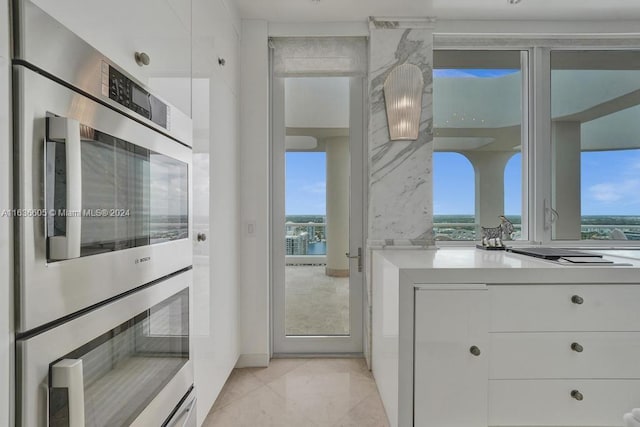 kitchen featuring light tile patterned flooring, stainless steel double oven, a healthy amount of sunlight, and white cabinets