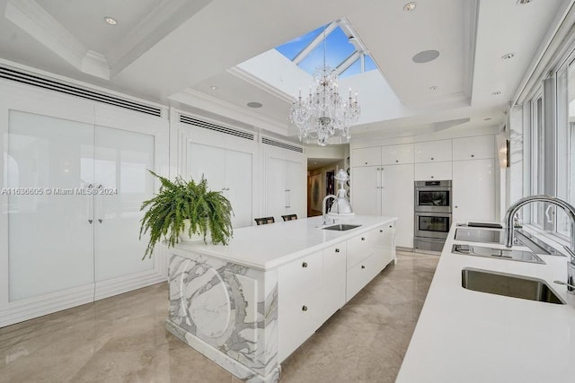 kitchen featuring double oven, an island with sink, sink, and a tray ceiling