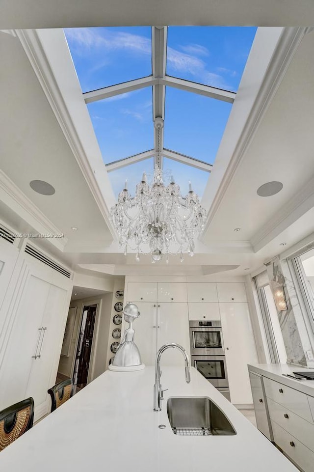 kitchen featuring a notable chandelier, white cabinetry, ornamental molding, sink, and stainless steel double oven