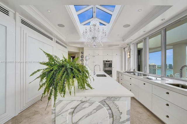 interior space featuring sink, a water view, a skylight, a tray ceiling, and a notable chandelier