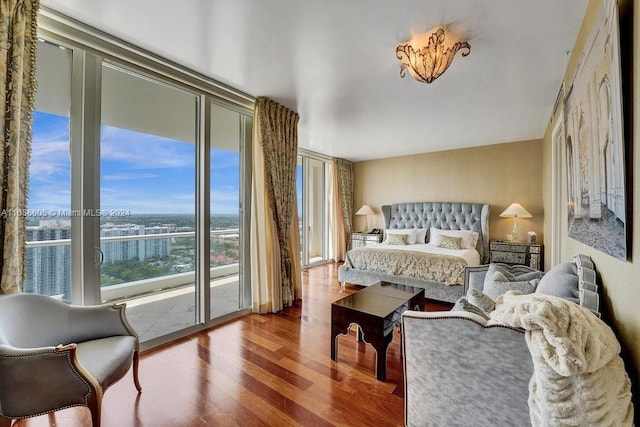 bedroom with hardwood / wood-style flooring, a wall of windows, a water view, and access to outside