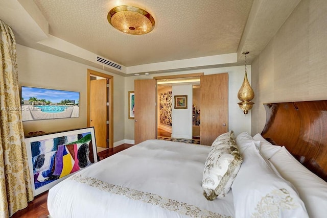 bedroom featuring dark wood-type flooring, a textured ceiling, and a raised ceiling