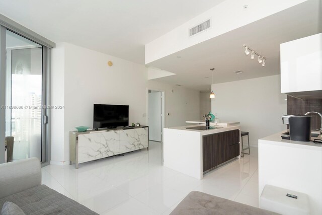 kitchen featuring dark brown cabinets, rail lighting, light tile patterned floors, decorative light fixtures, and sink