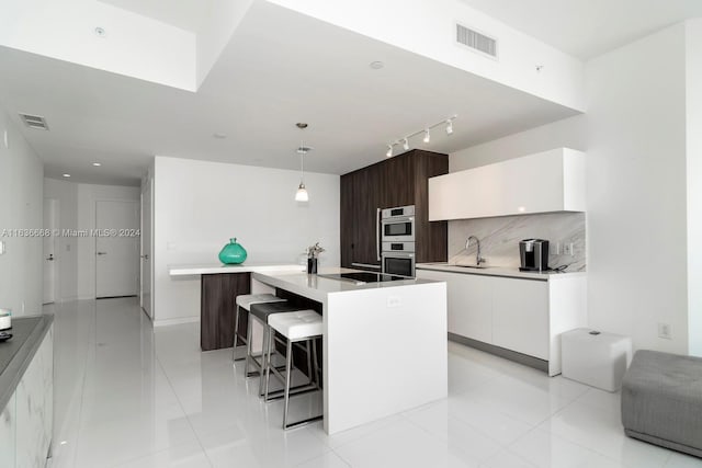 kitchen featuring an island with sink, decorative light fixtures, and white cabinets