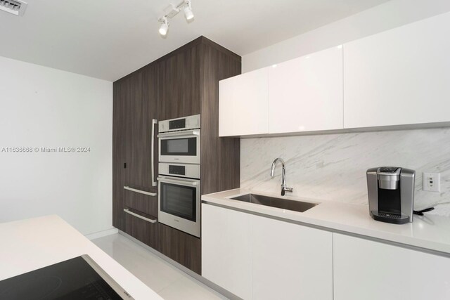 kitchen with sink, backsplash, dark brown cabinetry, white cabinetry, and double oven