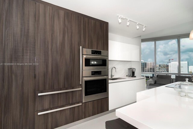 kitchen featuring dark brown cabinets, white cabinets, sink, stainless steel double oven, and track lighting