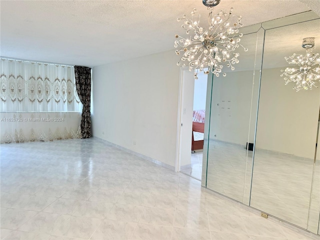 tiled spare room featuring a textured ceiling and an inviting chandelier