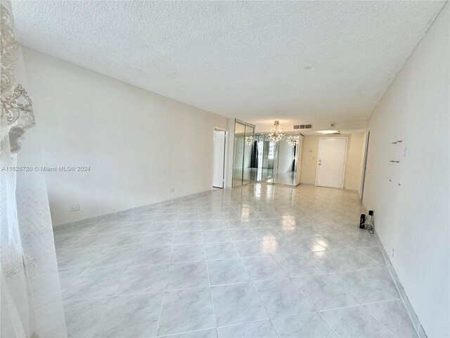 spare room with a textured ceiling, light tile patterned floors, and a chandelier