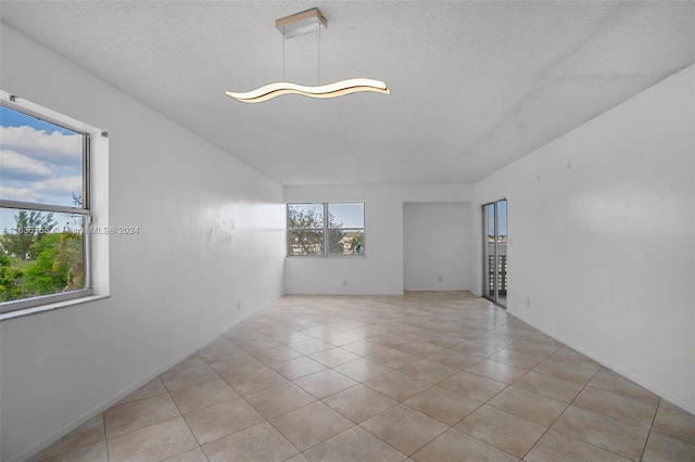 tiled empty room featuring a textured ceiling and a healthy amount of sunlight