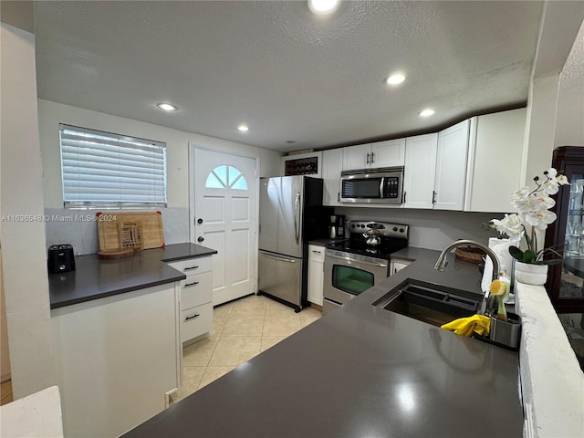 kitchen featuring sink, white cabinets, a textured ceiling, light tile patterned floors, and appliances with stainless steel finishes