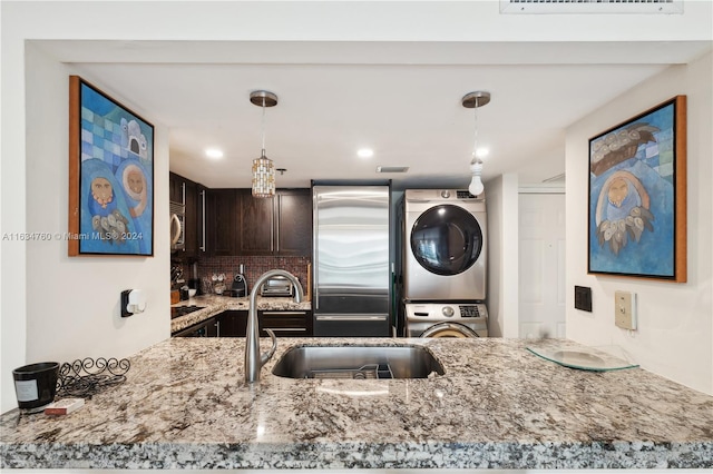 kitchen with decorative backsplash, appliances with stainless steel finishes, stacked washer and clothes dryer, and decorative light fixtures